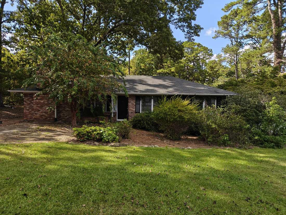 Overgrown shrubs and bare flower beds in front of a brick ranch home in Oconee County, GA, before trimming
